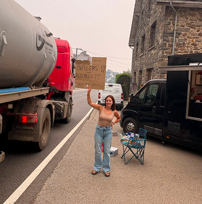 Helferin an der Straße in Robertville mit einem Schild: Burgers, Coca, Red Bull